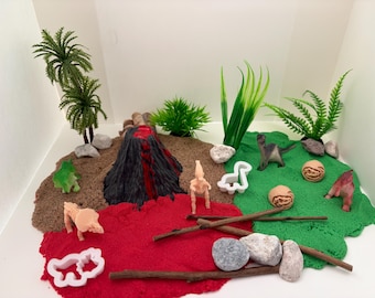 May include: A miniature dinosaur diorama featuring a volcano, palm trees, and various dinosaur figurines. The scene includes red, brown, and green textured surfaces, along with small rocks and wooden sticks. The dinosaurs are in various poses.