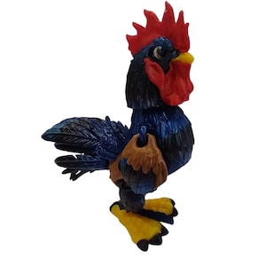 Könnte beinhalten: Eine blaue und braune Hahnfigur mit rotem Kamm und gelben Füßen. Der Hahn ist aus Kunststoff und hat eine strukturierte Oberfläche.