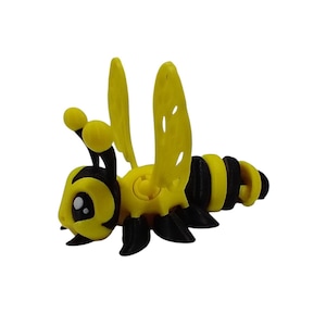 以下が含まれることがあります： 羽根とセグメント化された体を持つ黄色と黒の蜂のおもちゃ。蜂は大きな目をしたかわいい漫画の顔をしています。