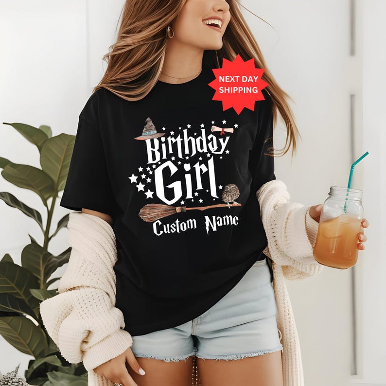 May include: Black t-shirt with a white graphic of a witch's hat, broom, owl, and the text "Birthday Girl" and "Custom Name".