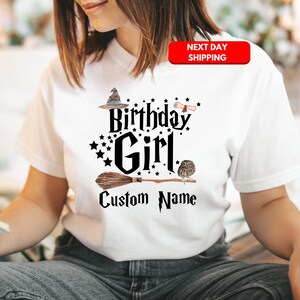 May include: White t-shirt with a black graphic design featuring a witch's hat, broom, owl, and the text "Birthday Girl" and "Custom Name".