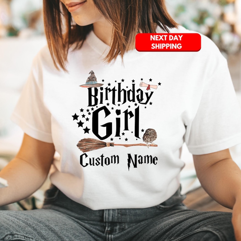 May include: White t-shirt with a black graphic design featuring a witch's hat, broom, owl, and the text "Birthday Girl" and "Custom Name".