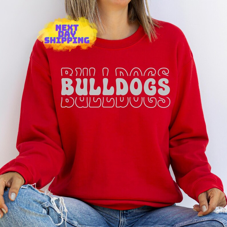 Op de afbeelding: Rood sweatshirt met de tekst "Run, Dog, Bulldogs" in een retro-lettertype.