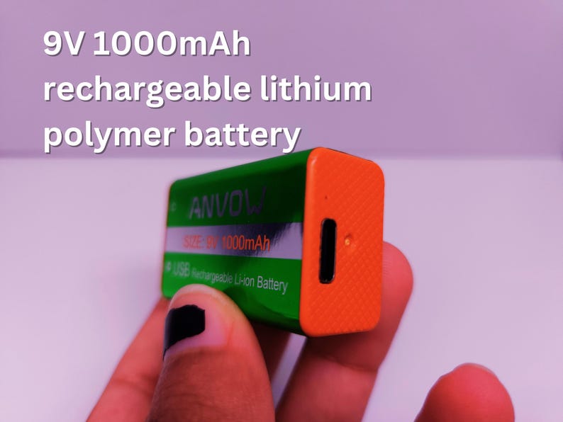 Close-up of a hand holding a green and orange ANVOW 9V 1000mAh rechargeable lithium polymer battery with a USB charging port. Overlaid text reads '9V 1000mAh rechargeable lithium polymer battery'