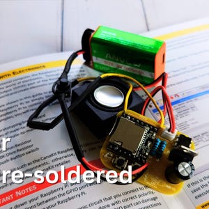 Pre-soldered DIY electronics project featuring a speaker, 9V battery, and a yellow PCB with components already mounted. The setup is placed on an open instruction manual. Overlaid text reads 'or Pre-soldered'.