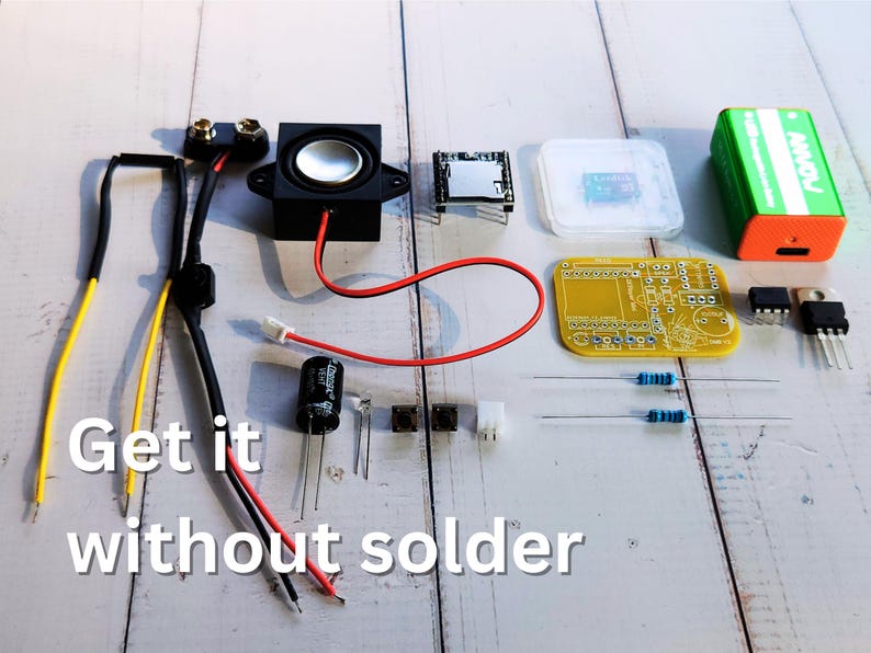 Electronics components for a DIY project neatly laid out on a wooden surface, including a speaker, battery clip, microcontroller, resistors, capacitors, a yellow PCB, push button, jumper wires, MOSFETs, and a 9V battery. Overlaid text reads 'Get it without solder'.