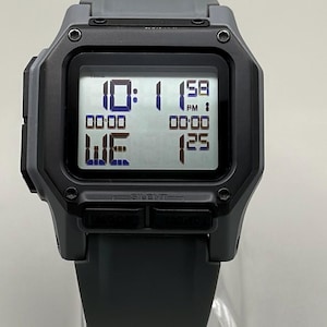 May include: A black digital wristwatch with a square face and a black rubber band. The watch face displays the time as 10:11 PM, the date as 00:00, and the day of the week as WE. The watch also has a SILENT button.