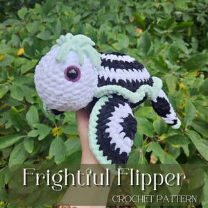 May include: A crocheted amigurumi turtle toy with a white and black striped shell and a green head. The toy has a single large eye and is called "Frightful Flipper" Crochet Pattern.