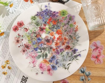 Op de afbeelding: Een wit bord met verschillende aquarelbloemenstickers. De stickers tonen verschillende soorten bloemen in tinten roze, blauw, paars en oranje.