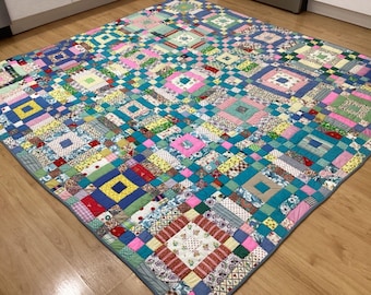 May include: A large patchwork quilt with a variety of colorful squares and rectangles. The quilt is made of different fabrics and patterns, including floral, geometric, and plaid. The quilt is edged with a light blue fabric.