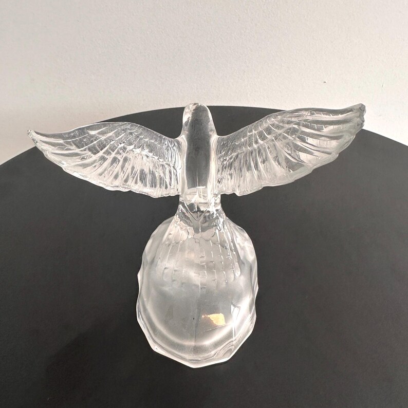 Puede incluir: Una escultura de cristal transparente de una paloma con las alas extendidas. La paloma est&aacute; posada sobre una base redonda.
