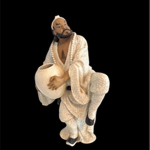 Peut inclure: Une figurine en céramique blanche représentant un homme vêtu d'un costume traditionnel chinois tenant une jarre en céramique blanche. La figurine a un visage détaillé avec une barbe et porte une robe blanche avec un collier de perles.