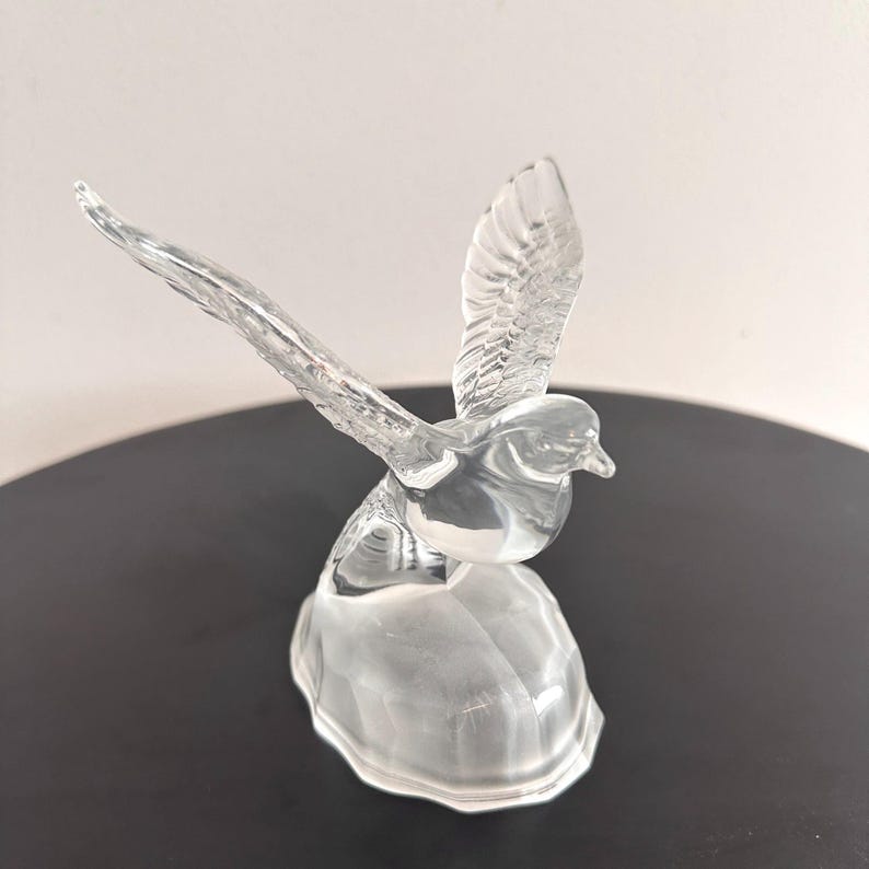 Puede incluir: Una figurita de cristal transparente de un p&aacute;jaro en vuelo con las alas extendidas. El p&aacute;jaro est&aacute; posado sobre una peque&ntilde;a base de cristal transparente.