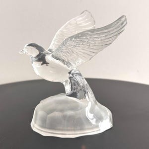 Puede incluir: Una figurita de paloma de cristal transparente con las alas extendidas. La paloma est&aacute; posada sobre una peque&ntilde;a base de cristal transparente.