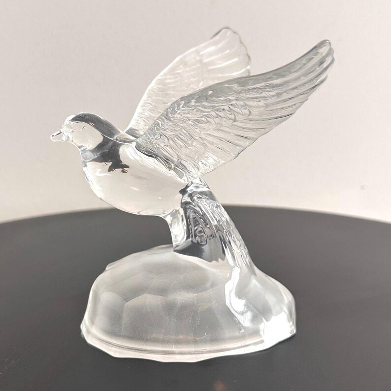Puede incluir: Una figurita de paloma de cristal transparente con las alas extendidas. La paloma est&aacute; posada sobre una peque&ntilde;a base de cristal transparente.