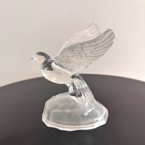 Puede incluir: Una figurita de paloma de cristal transparente con las alas extendidas, posada sobre una peque&ntilde;a base de cristal transparente.