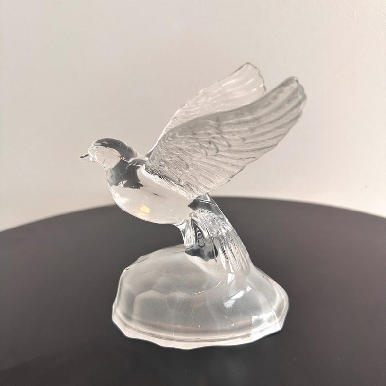 Puede incluir: Una figurita de paloma de cristal transparente con las alas extendidas, posada sobre una peque&ntilde;a base de cristal transparente.