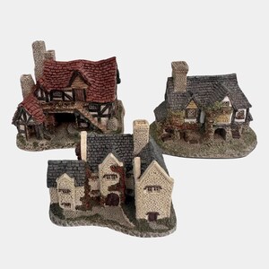 May include: Three miniature village houses with detailed features. One has a red tiled roof and a chimney. Another has a gray tiled roof and a sign that reads "Hogs Head". The third house has a gray tiled roof and a stone facade.