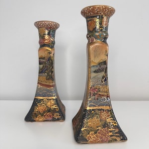 May include: A pair of vintage Japanese candlestick holders with intricate gold and black floral designs. The holders are made of ceramic and feature a traditional Japanese scene with a woman in a kimono.