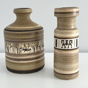 May include: Two ceramic vases with a striped pattern in shades of brown and white. The larger vase has a geometric design in black and white. The smaller vase has a black and white geometric design with a stylized figure.