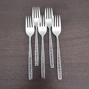 Peut inclure: Six fourchettes argentées avec un motif floral sur les manches, disposées sur une surface en bois brun foncé. Les fourchettes sont en métal brillant.