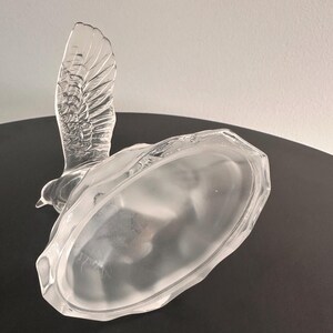 Puede incluir: Una figurita de p&aacute;jaro de vidrio transparente con un acabado esmerilado. El p&aacute;jaro est&aacute; en posici&oacute;n de vuelo con las alas extendidas. La base de la figurita es de forma ovalada esmerilada.