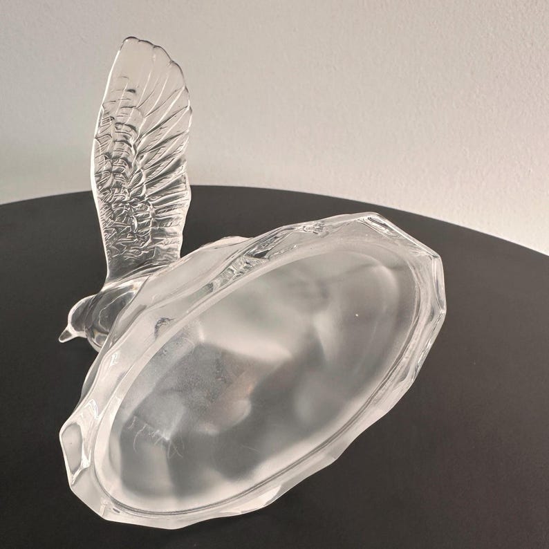 Puede incluir: Una figurita de p&aacute;jaro de vidrio transparente con un acabado esmerilado. El p&aacute;jaro est&aacute; en posici&oacute;n de vuelo con las alas extendidas. La base de la figurita es de forma ovalada esmerilada.