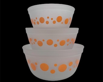 May include: A stack of three frosted white mixing bowls with orange polka dots. The bowls are nested, with the largest bowl at the bottom and the smallest at the top. The bowls have a simple, rounded design and are set against a black background.