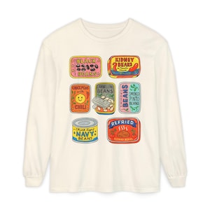 Könnte beinhalten: Ein cremefarbenes Langarmshirt mit einem bunten Grafikdruck verschiedener Bohnendosen. Die Etiketten enthalten Texte wie Black Beans, Kidney Beans, Chickpeas with Chili, Cannellini Beans, Smoked Pinto Beans, Navy Beans und Refried Beans.