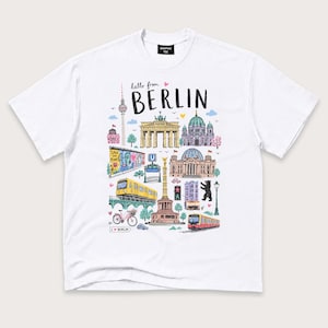 May include: A white short-sleeve t-shirt featuring a colourful graphic print of Berlin landmarks including the TV Tower, Brandenburg Gate, and Berlin Cathedral. The text reads "hello from BERLIN" with small pink hearts and an "I love BERLIN" sign.
