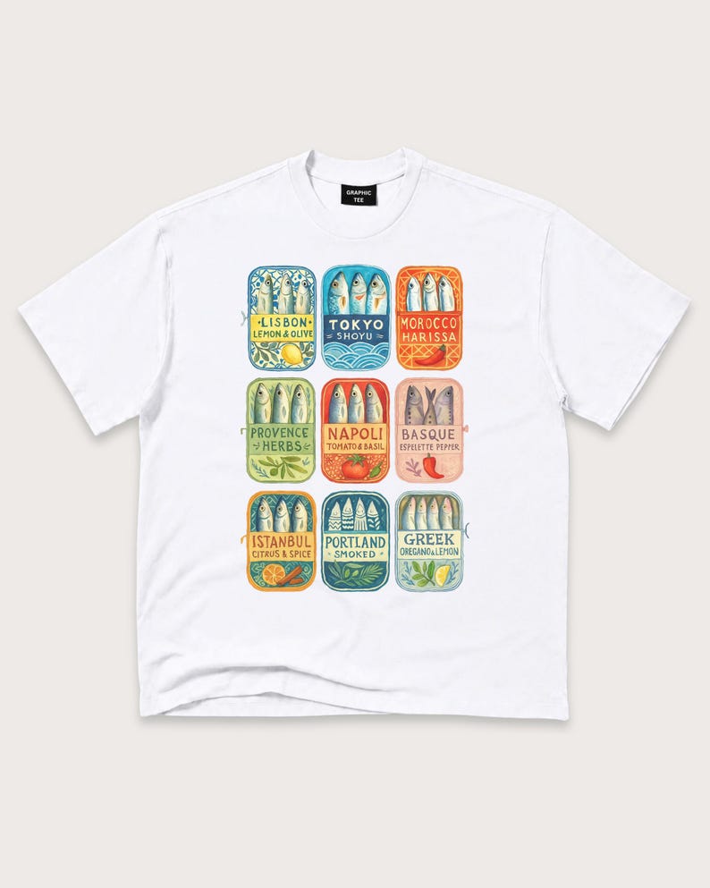 May include: A white short-sleeve t-shirt featuring a graphic print of nine rectangular sardine tin illustrations. Each tin displays a different city name, flavor profile, and fish arrangement, including Lisbon, Tokyo, Morocco, Provence, Napoli, Basque, Istanbul, Portland, and Greek.