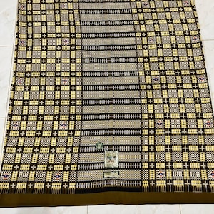 以下が含まれることがあります： 緑色の小さなラベルが付いた、茶色と黄色の模様の布。布は、プラス記号の繰り返し模様のある格子模様です。