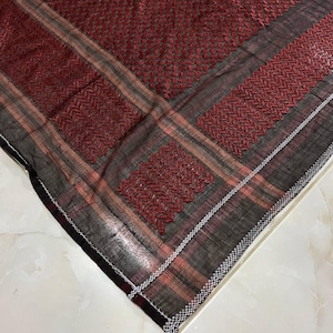 Puede incluir: Una bufanda de patrón rojo y negro con un borde blanco. La bufanda está hecha de un tejido fino y tejido y tiene un borde con flecos.