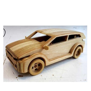 Puede incluir: Un coche de juguete de madera con un acabado marrón claro. El coche presenta un diseño detallado, que incluye ruedas, ventanas y espejos laterales. La carrocería del coche tiene un patrón de rayas en el capó. Este coche de juguete artesanal es un gran regalo.