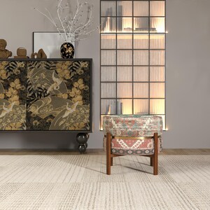 a modern living room with a black and gold cabinet, a patterned ottoman, and a glass-paneled wall.