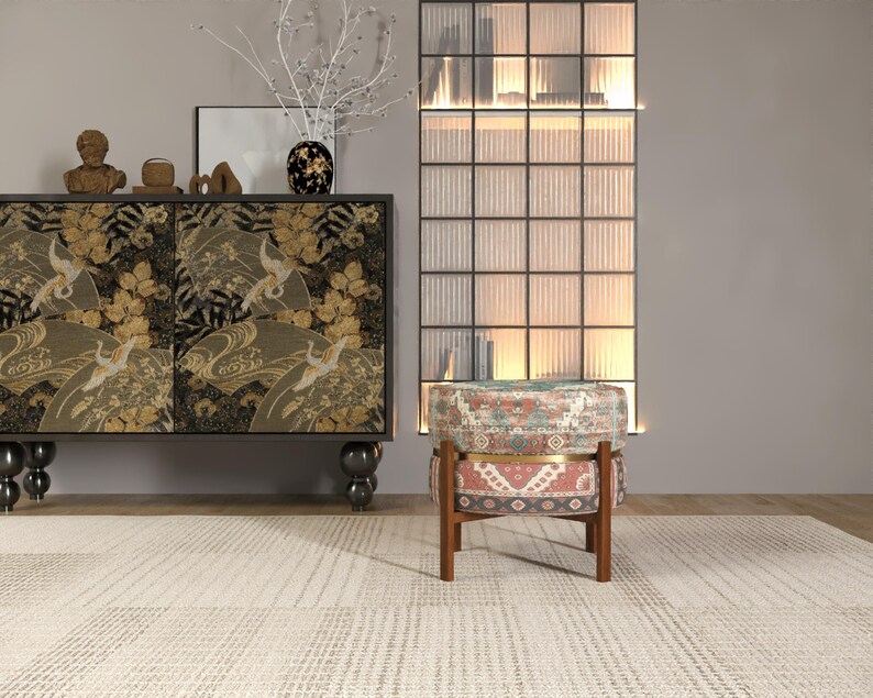 a modern living room with a black and gold cabinet, a patterned ottoman, and a glass-paneled wall.