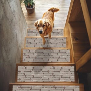 Pode incluir: Um cão Golden Retriever desce uma escada de madeira com degraus decorativos. Os degraus da escada têm um fundo cinza claro com um padrão repetitivo de elementos decorativos castanhos e brancos.