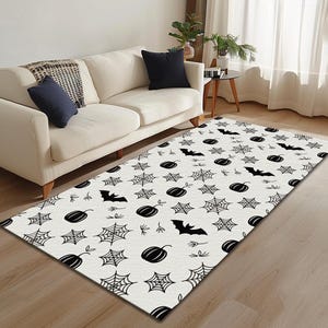 May include: A rectangular Halloween-themed rug with a white background and a repeating pattern of black pumpkins, spiderwebs, and bats. The rug is placed on a wooden floor in a living room setting.