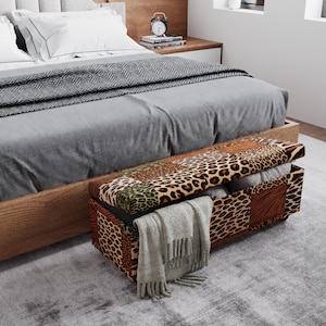 May include: A bed with a gray comforter and a patterned storage bench at the foot. The bench features a patchwork design with animal print and brown accents. A gray blanket is draped over the bench.
