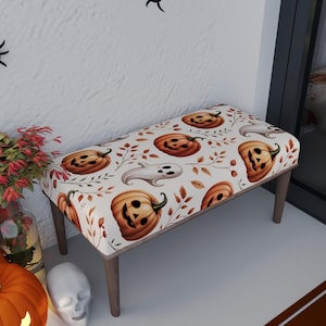 May include: A rectangular bench with a Halloween-themed pattern. The bench features a white background with orange jack-o'-lanterns, ghosts, and autumn leaves. The wooden legs provide support. The bench is designed for indoor use.