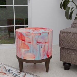 May include: A round, pink and blue ottoman with a jellyfish print. The ottoman has wooden legs.