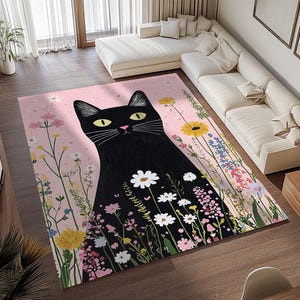 Op de afbeelding: Een roze en zwart vloerkleed met een zwarte kat illustratie omringd door kleurrijke bloemen. De kat heeft gele ogen en kijkt recht naar de kijker.