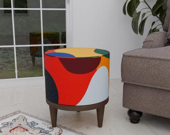 Puede incluir: Un puf colorido con estampado abstracto, base de madera y cuatro patas. El puf es rojo, amarillo, azul, verde y blanco.