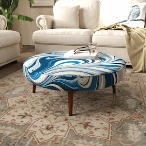 May include: A round ottoman featuring a swirling marbled pattern in shades of deep blue, light blue, and white. The piece is supported by four tapered wooden legs in a medium brown finish, providing a stable base for the upholstered circular seat.