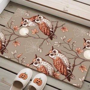 May include: A rectangular doormat featuring a detailed illustration of owls perched on branches with autumn leaves and spiderwebs. The owls have brown and white feathers. Two pairs of pumpkin-themed slippers are at the bottom.