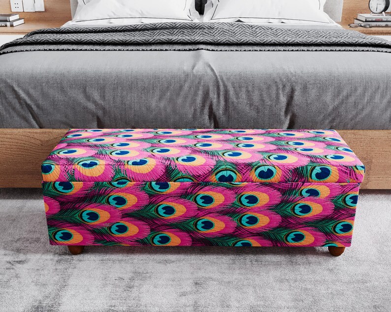 A colorful ottoman with a pattern of peacock feathers is placed in front of a bed, creating a vibrant and eye-catching display.