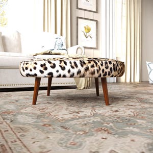 a leopard print ottoman with a wooden base, placed on a patterned rug in a living room setting.