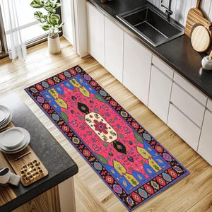 May include: A rectangular runner rug with a vibrant pink central field. The rug features a detailed border with blue, yellow, and black geometric patterns. The central design includes floral and leaf motifs, creating a colorful and decorative accent.
