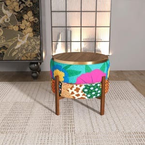 May include: A round ottoman with a dark wood top and a gold metal rim. The base features a vibrant, multi-patterned fabric upholstery with floral, animal print, and geometric designs in bright colors, supported by four straight dark wood legs.