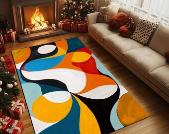 Op de afbeelding: Een rechthoekig vloerkleed met een abstract ontwerp in blauw, oranje, geel, wit en zwart. Het kleed ligt op een houten vloer in een woonkamer met een open haard en kerstboom op de achtergrond.